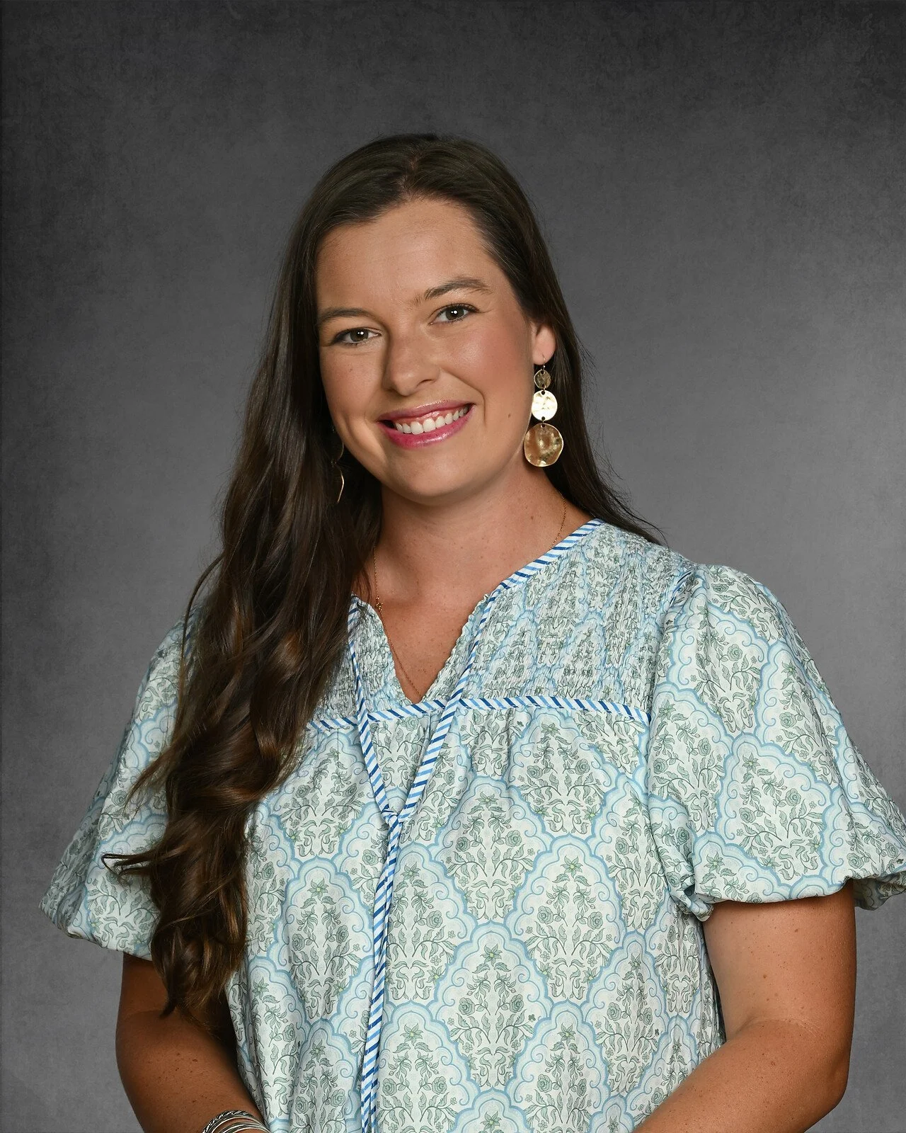 Smiling woman with long dark hair wearing a colorful plaid dress against a gradient background.