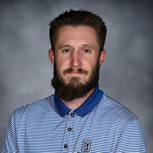 Man with a beard wearing a black suit, white shirt, and black tie, smiling at the camera.