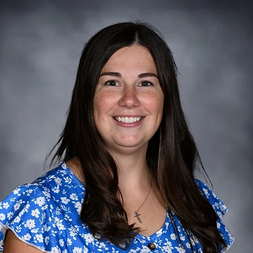 Person with long brown hair wearing a white shirt, smiling against a dark background.