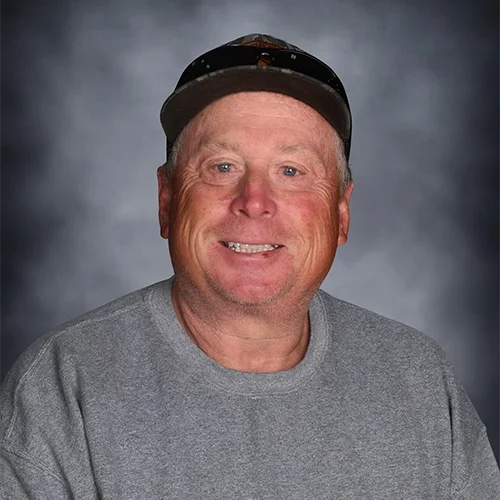 A smiling man wearing a gray baseball cap and a light blue T-shirt against a gray background.