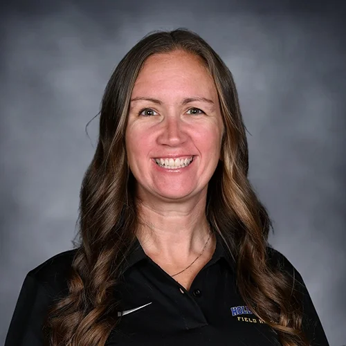 Woman with long hair wearing a maroon polo shirt with "Eagles" logo, smiling against a gray background.