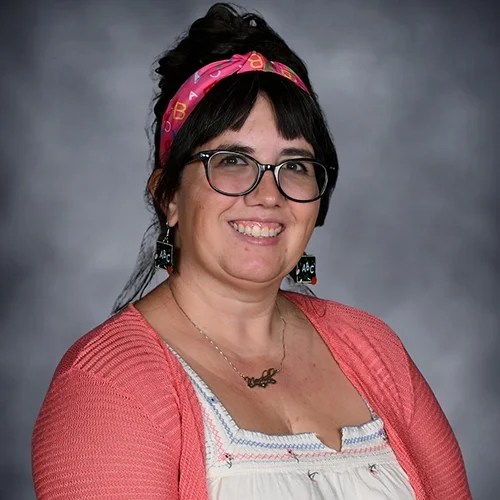 Smiling person wearing glasses and parrot-shaped earrings.