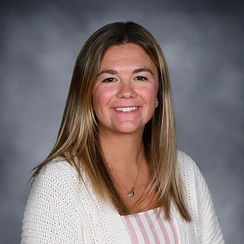 Portrait of a smiling person with long hair wearing a white shirt against a dark background.