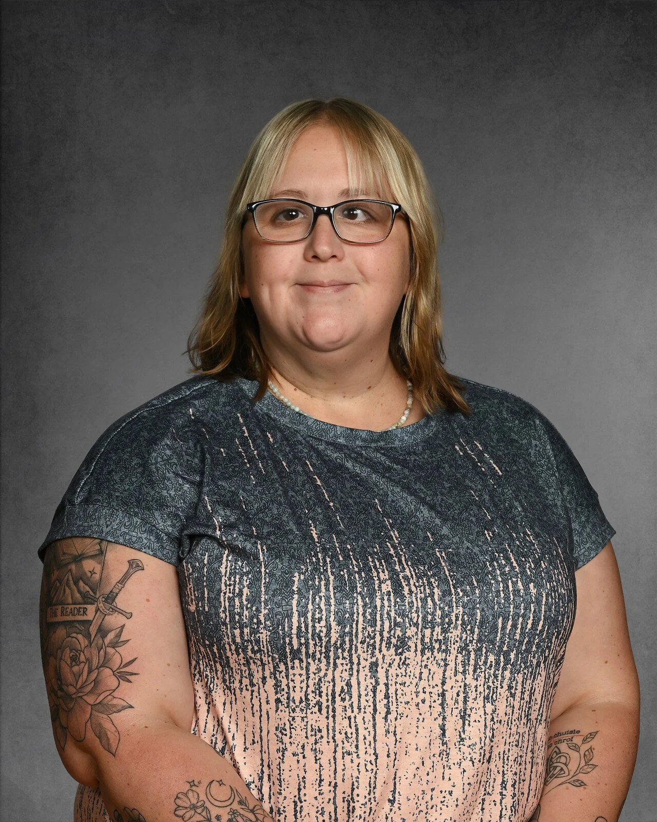 Portrait of a woman with blonde and dark brown hair, wearing glasses and a green sweater, against a gray background.