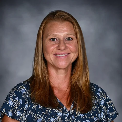 A professional portrait of an African American woman wearing a black top and multiple strands of pearl necklaces, smiling against a dark background.