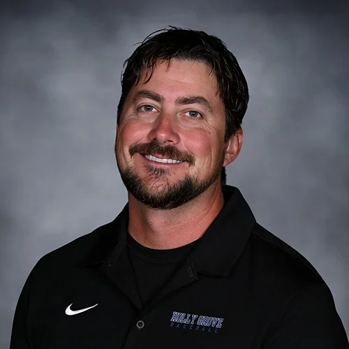 A man with dark hair and a beard wearing a charcoal gray polo shirt with the logo of Holly Grove Christian School Athletics, smiling against a dark gray background.