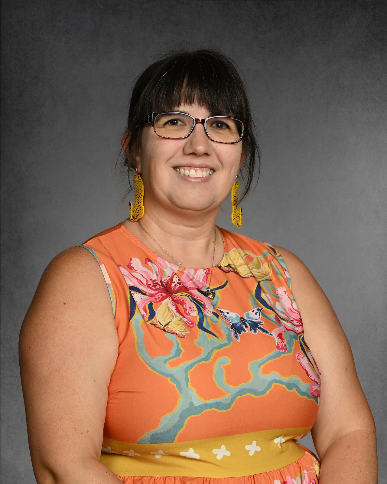 Smiling person wearing glasses and parrot-shaped earrings.