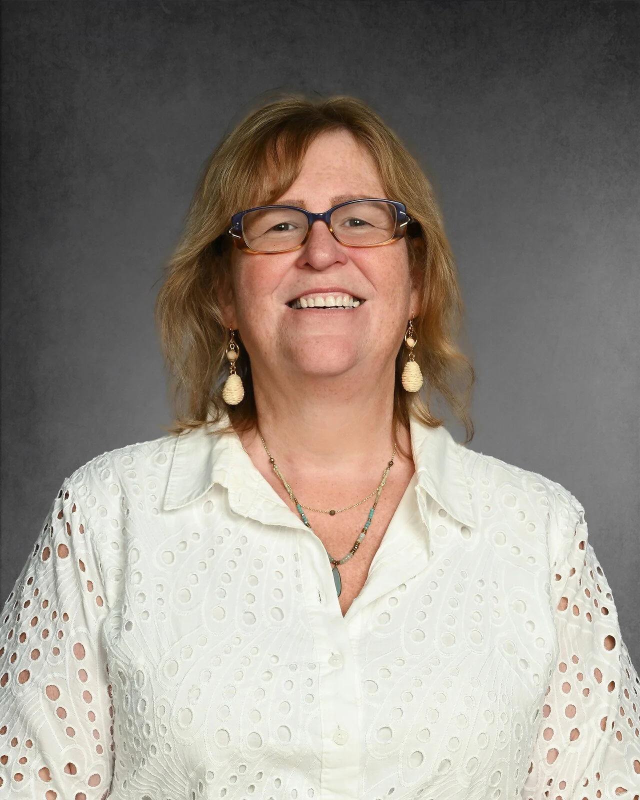 Person wearing glasses and a floral-patterned blouse, smiling against a gray background.