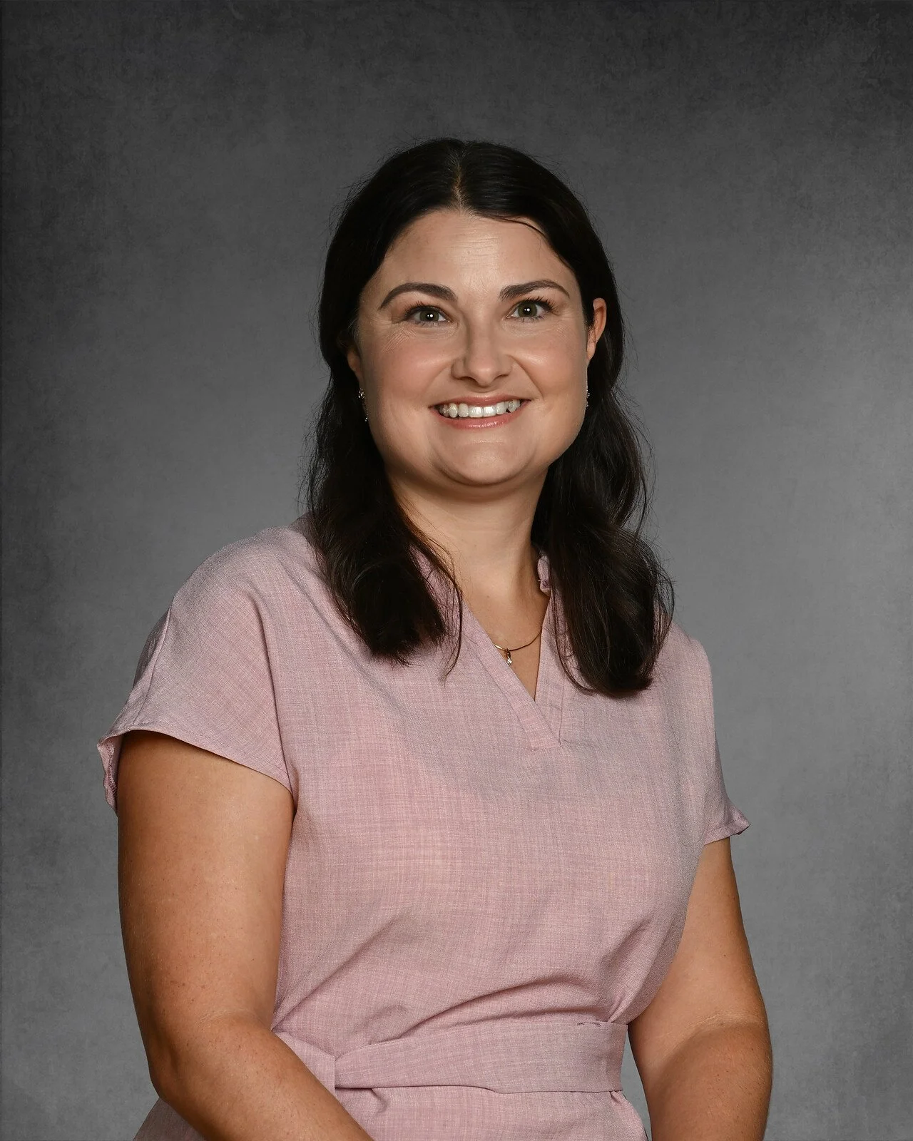 Woman with dark hair wearing a floral blouse on a gray background.