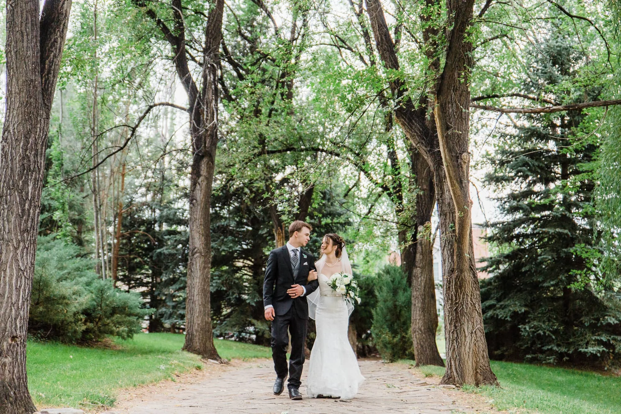 Couple walking arm in arm down a tree covered path.