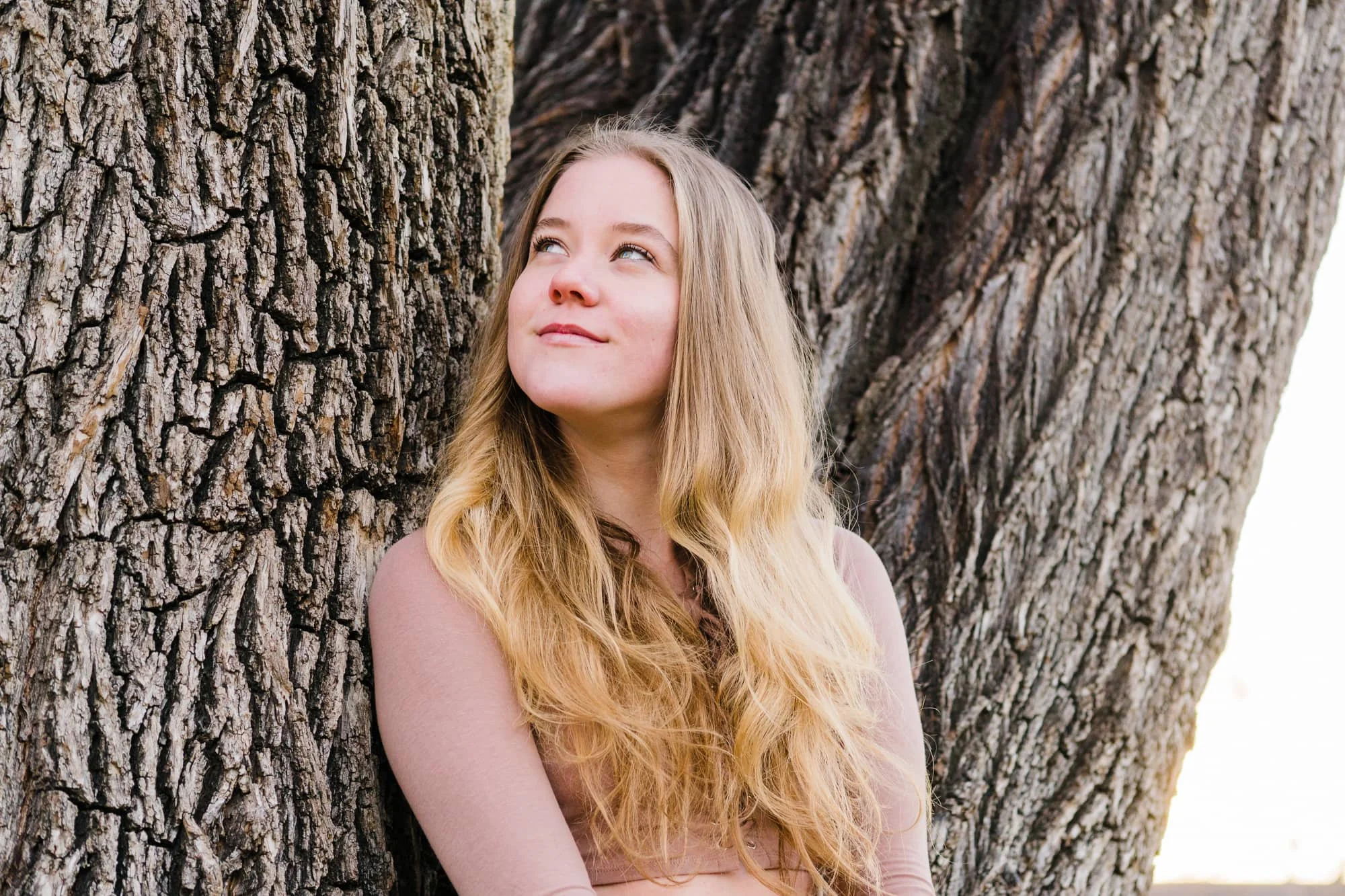 Portrait of woman leaning against tree and looking up in a playfully thoughtful way.