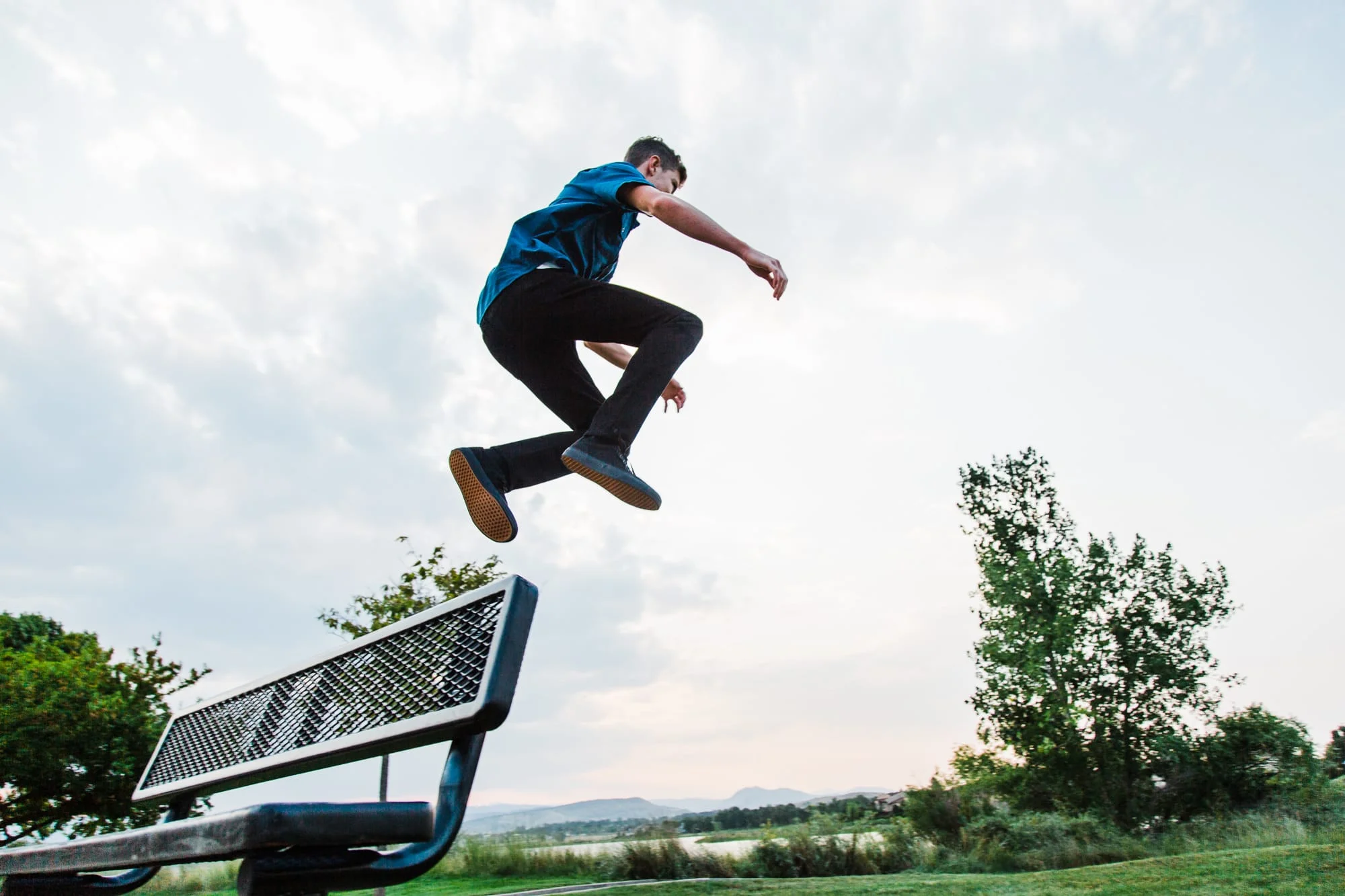 Wide shot of a high school senior guy jumping off the back of a bench.