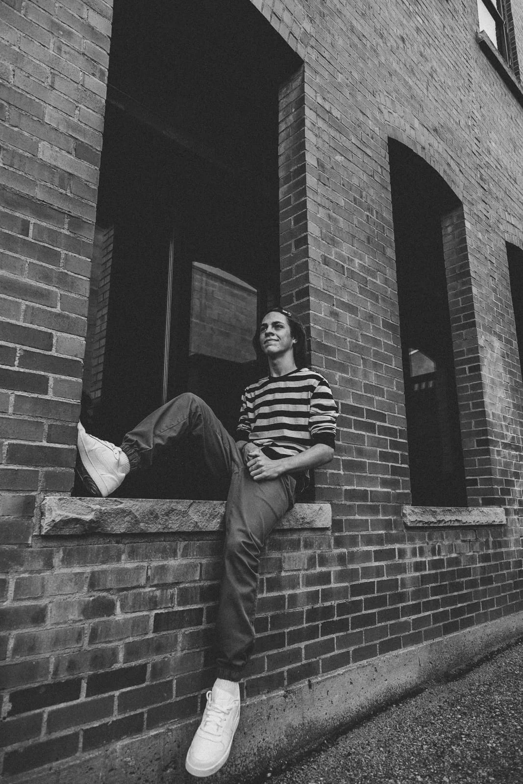 Wide portrait of a young man sitting on a ledge and letting one leg dangle, in black and white.