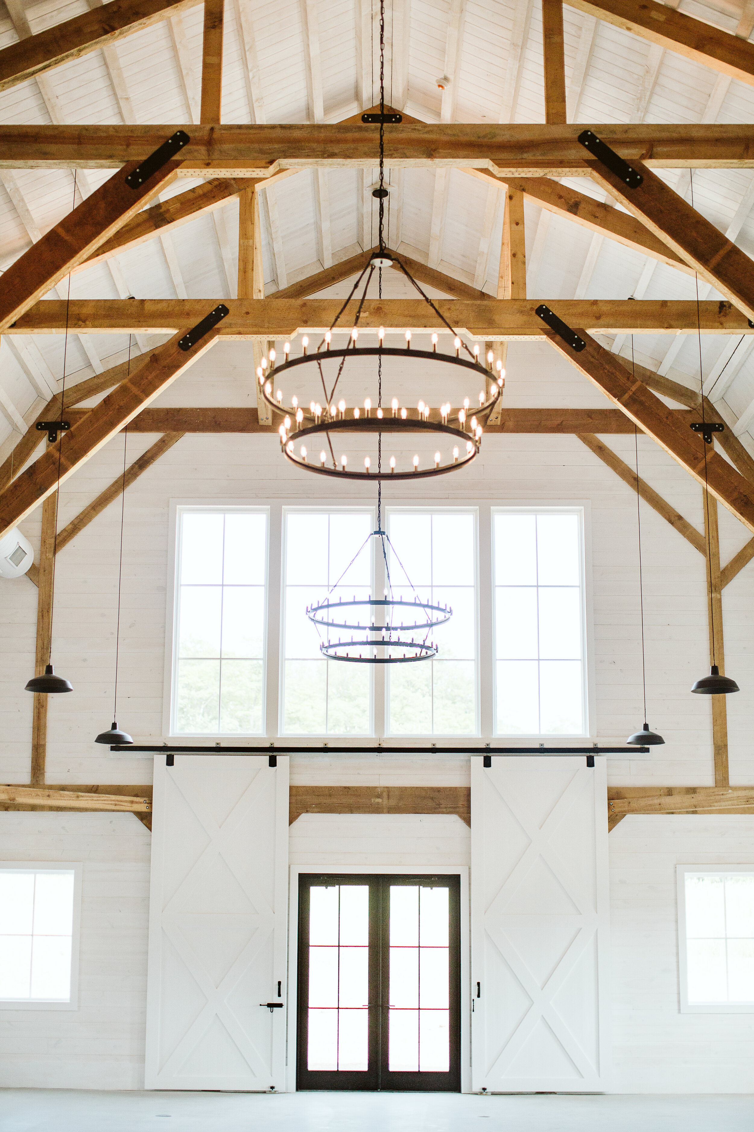  [PHOTO] A wider view of the barn doors in the Gambrel Room with large picture windows above and one of three chandeliers 