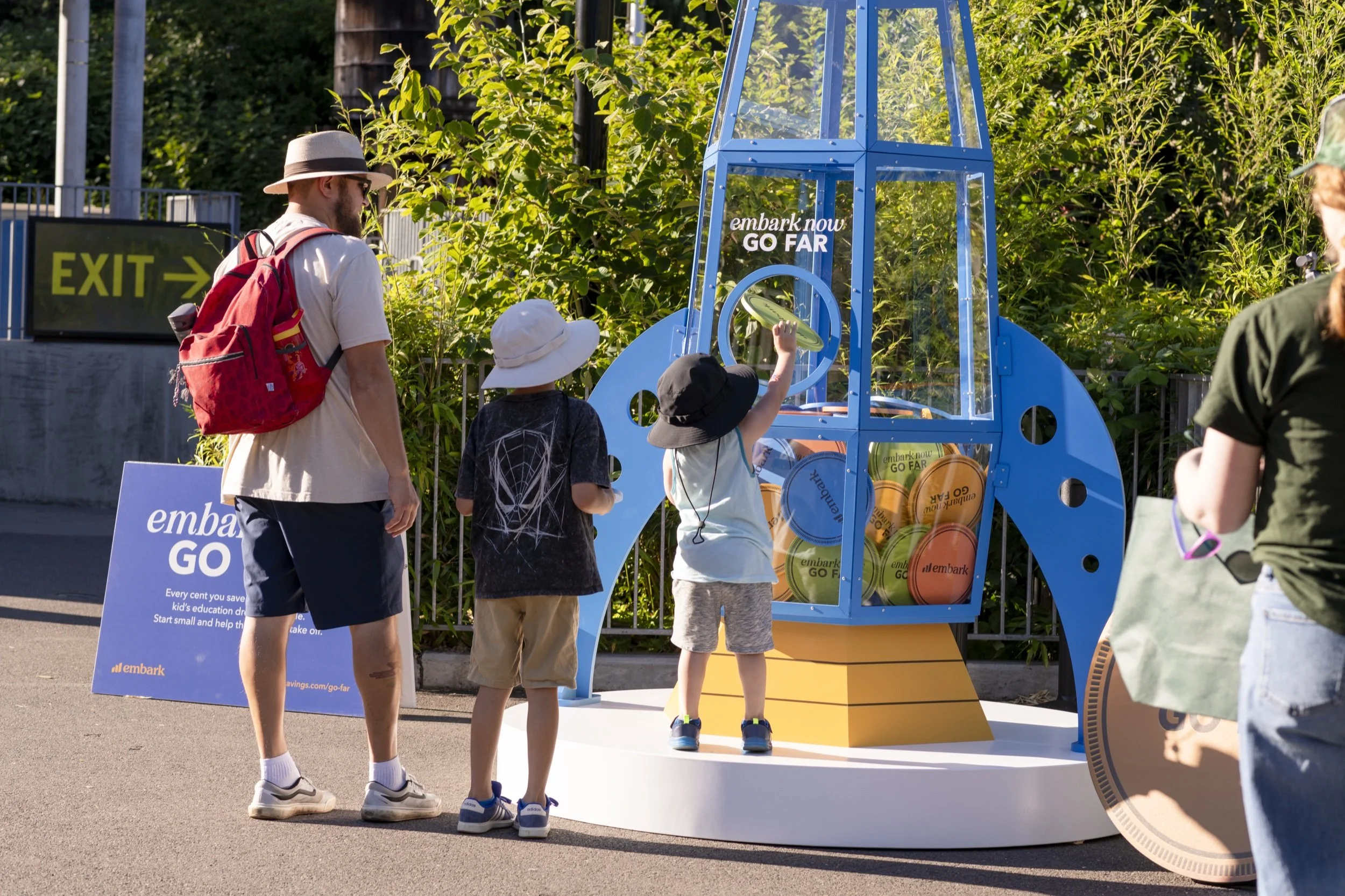 Children place oversized branded coins into the Embark rocket installation at the Oregon Zoo.