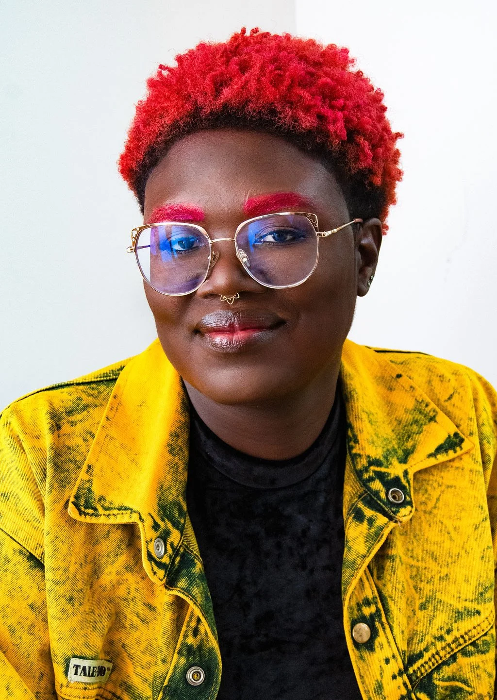 Black person with short red hair and eyebrows, with glasses and a yellow shirt.