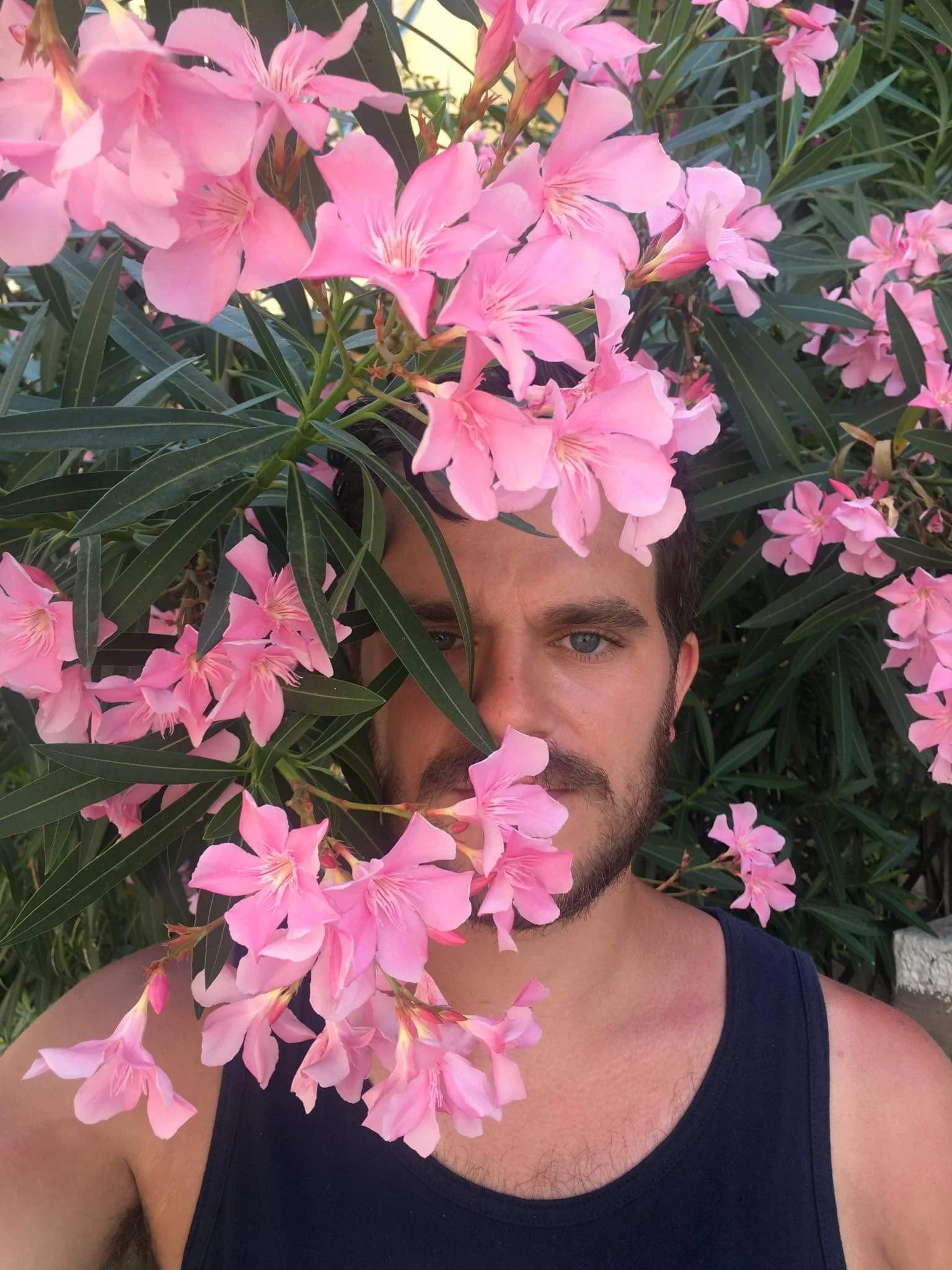 White man slightly obscured by pink flowers, wearing a black tank top.