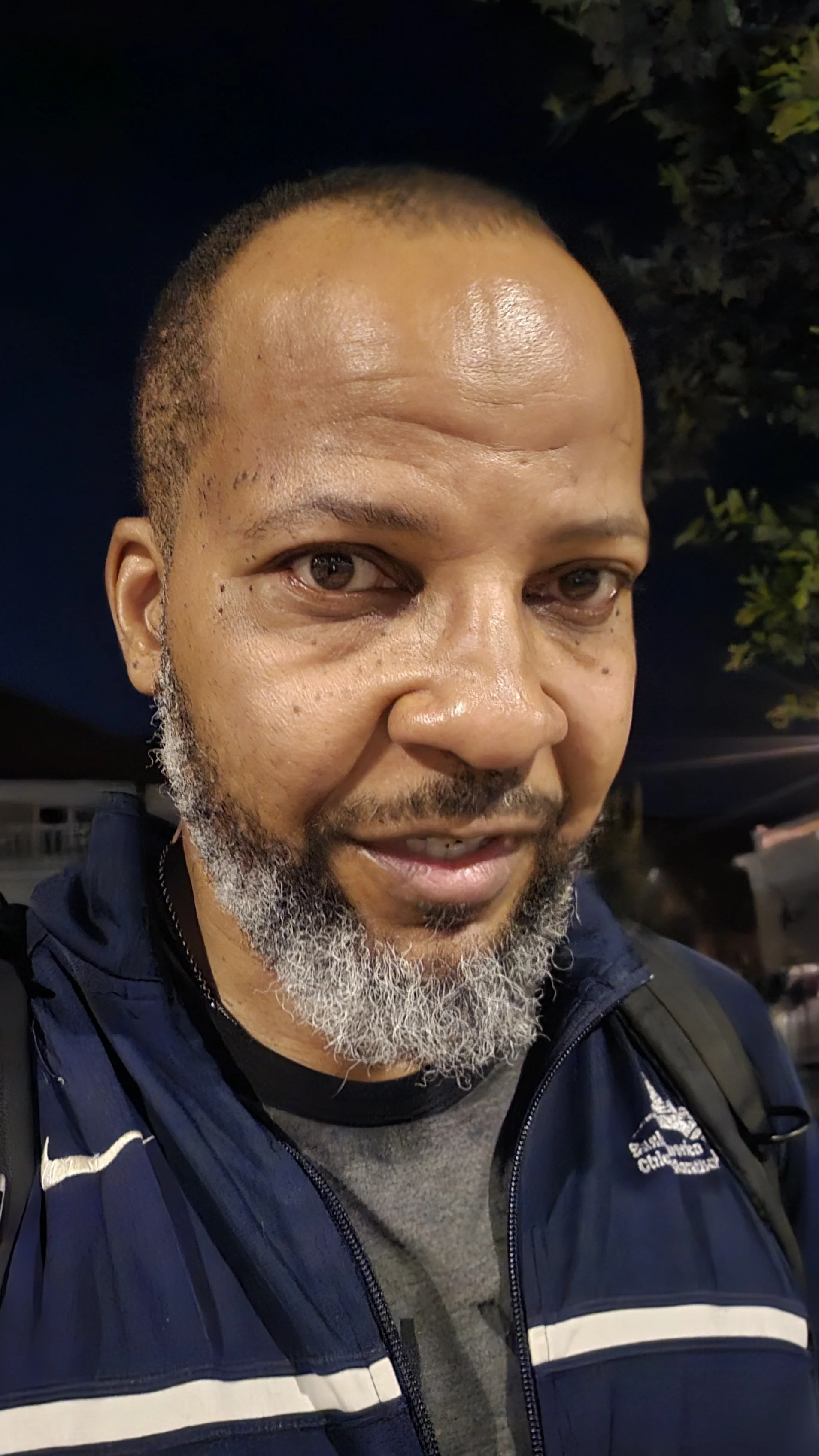 Man with grey beard and dark collar shirt looking to camera.