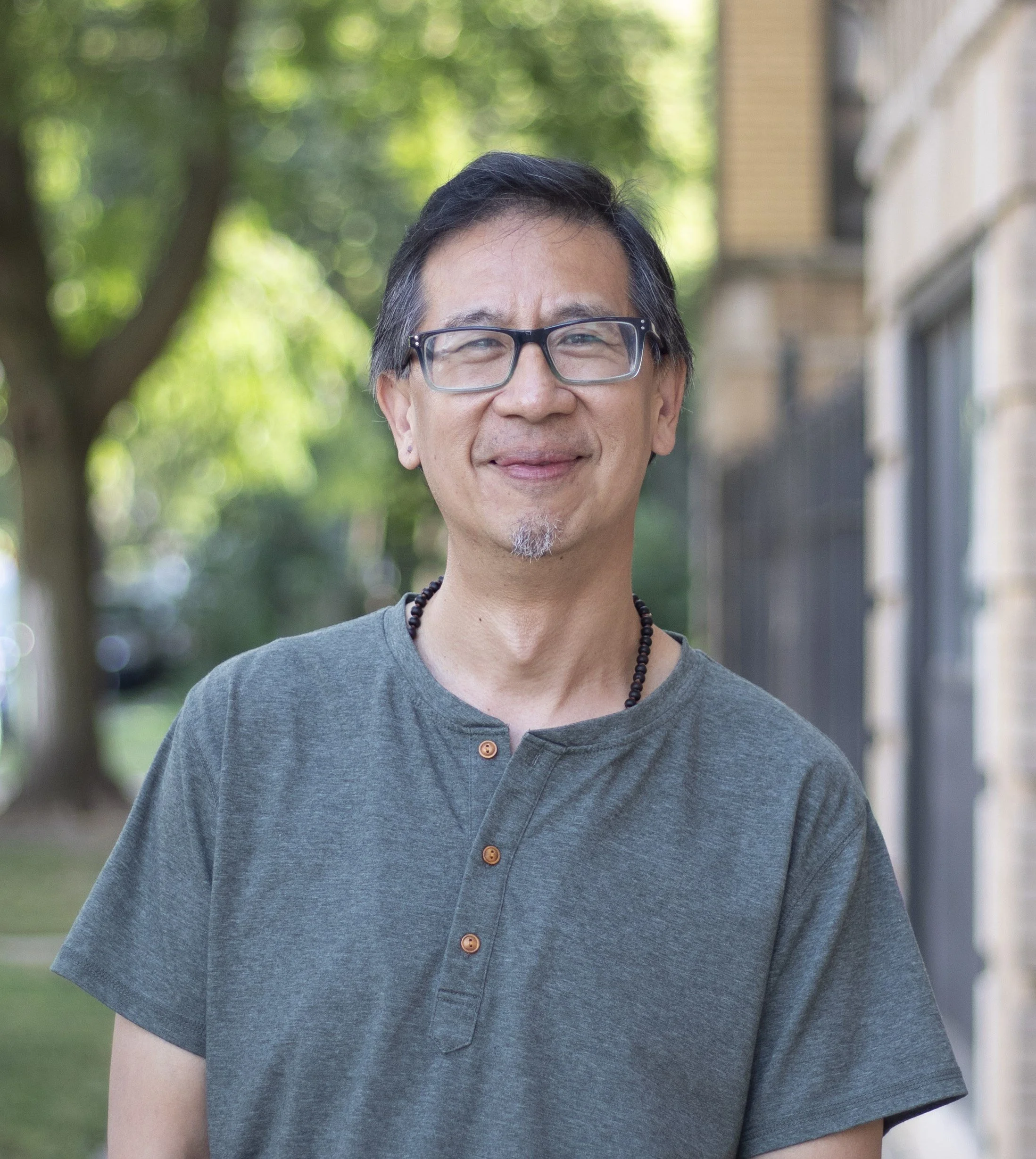 Chinese-American man wearing grey shirt and glasses, with dark hair smiling to camera.
