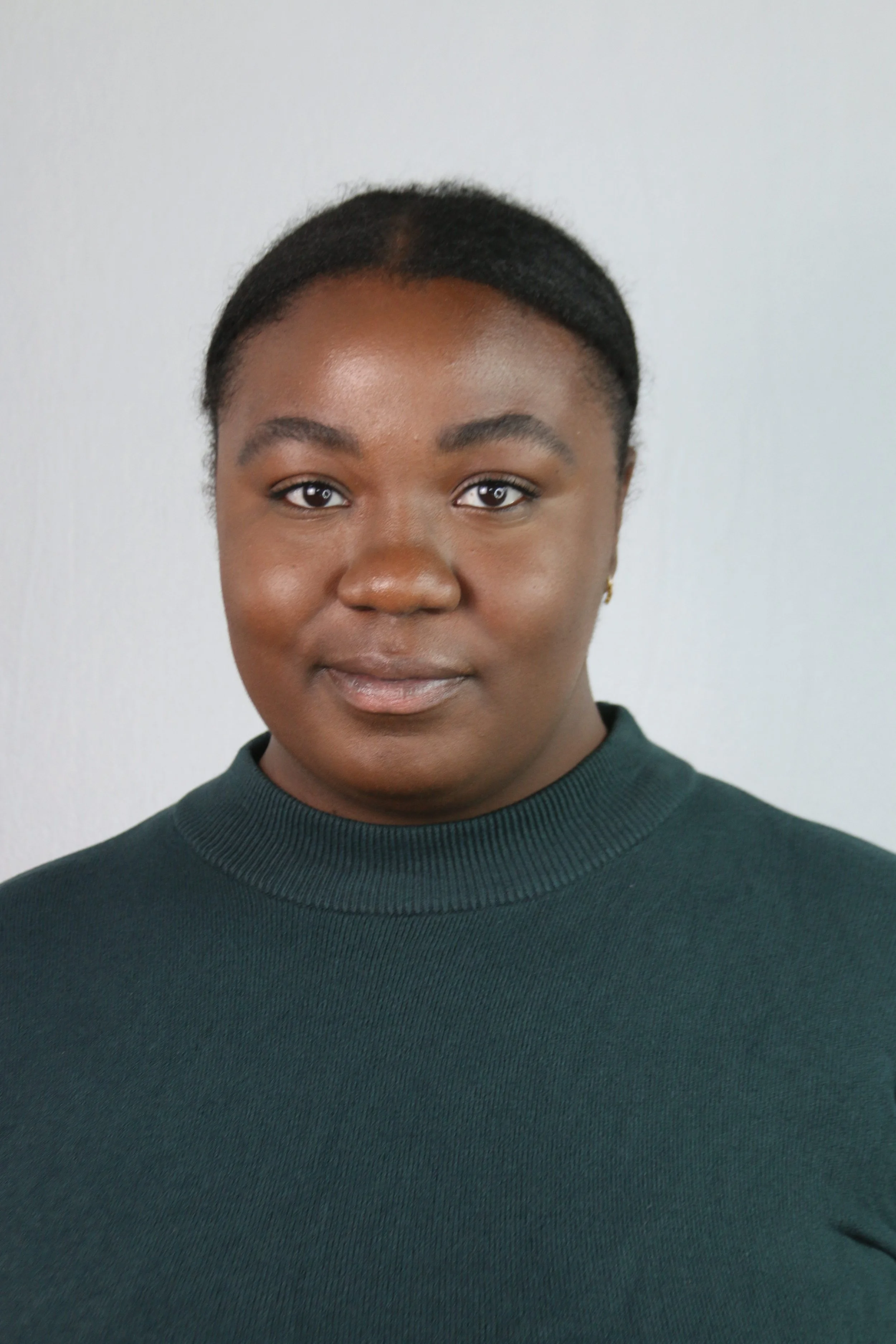 Young woman with brown skin, smiling to camera with dark hair pulled back.