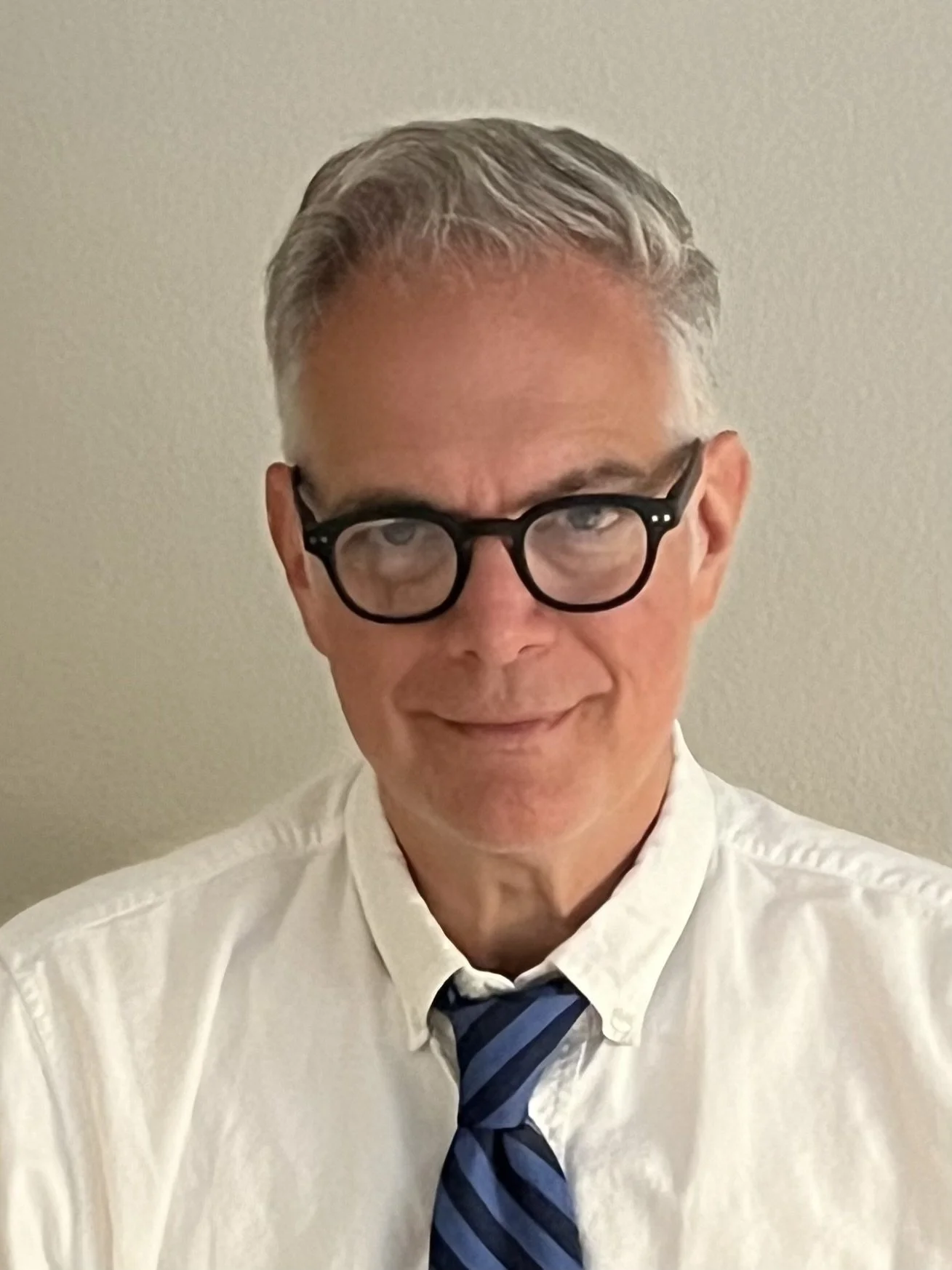 White man with grey hair, black rimmed glasses, and white shirt.