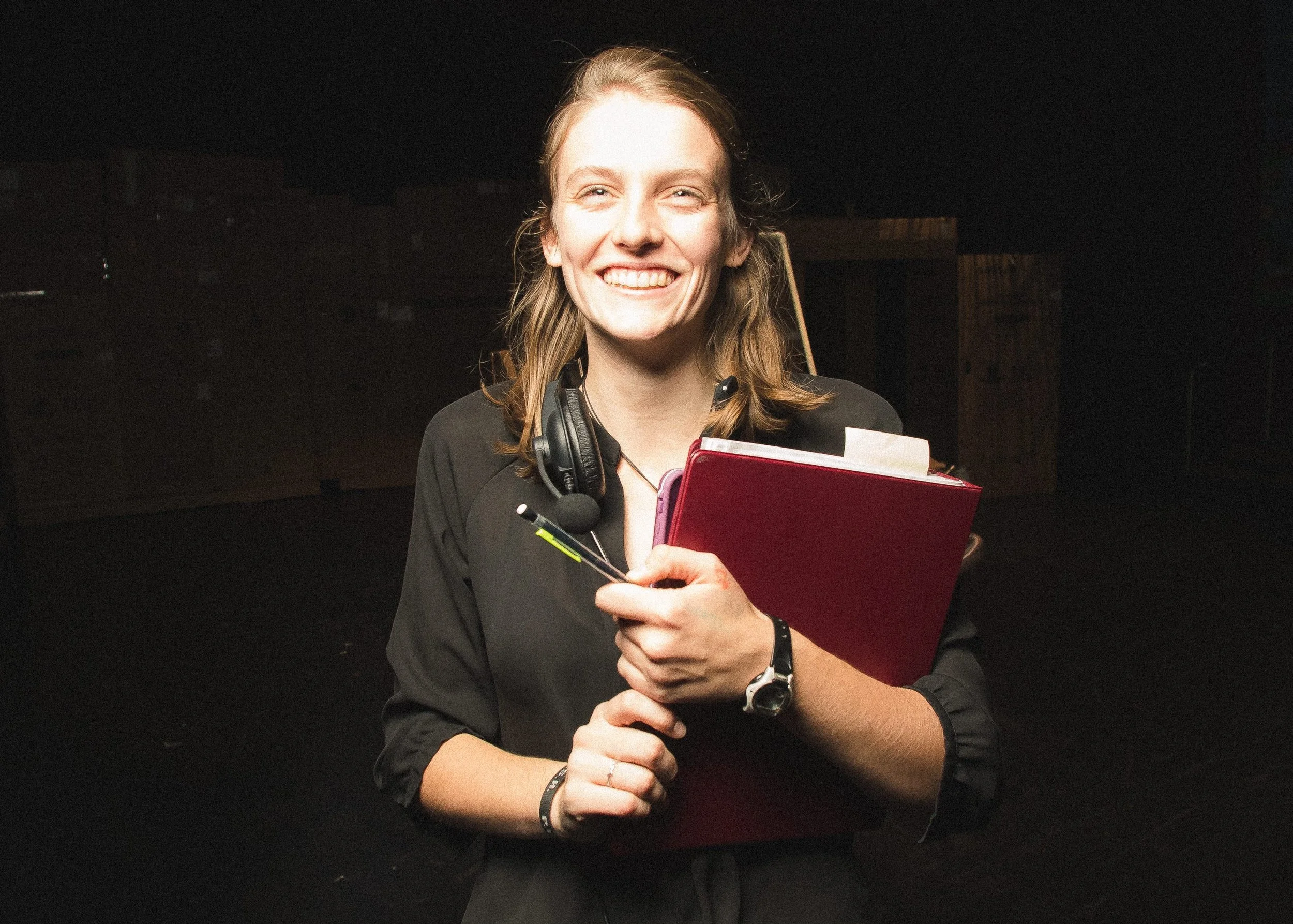 White woman wearing black shirt holding a red folder, with shoulder length blonde hair and smiling to camera.