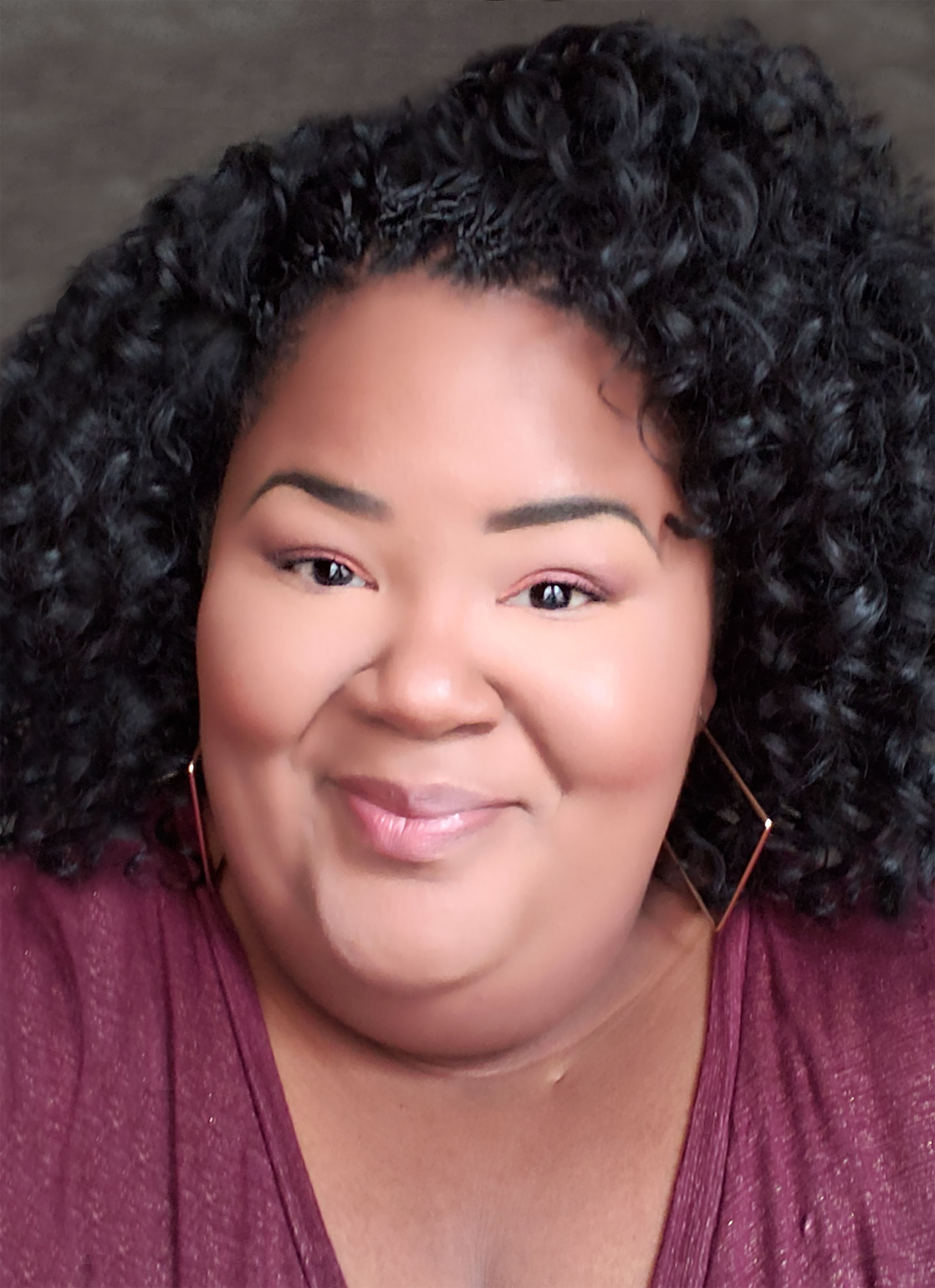 Black woman with curly dark hair, smiling and wearing rectangle earrings.