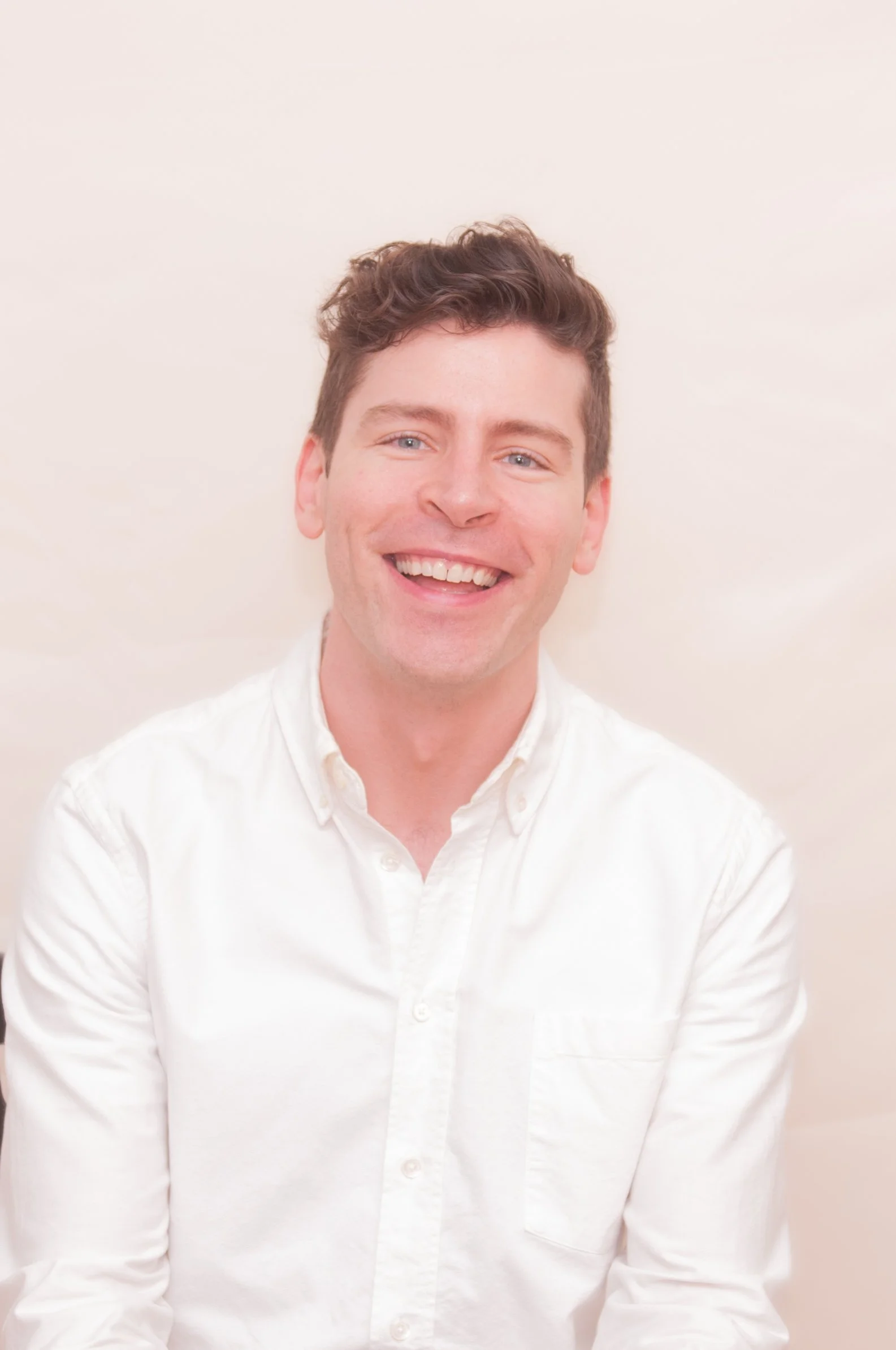White man with light brown short hair, wearing white button down shirt, smiling to camera.