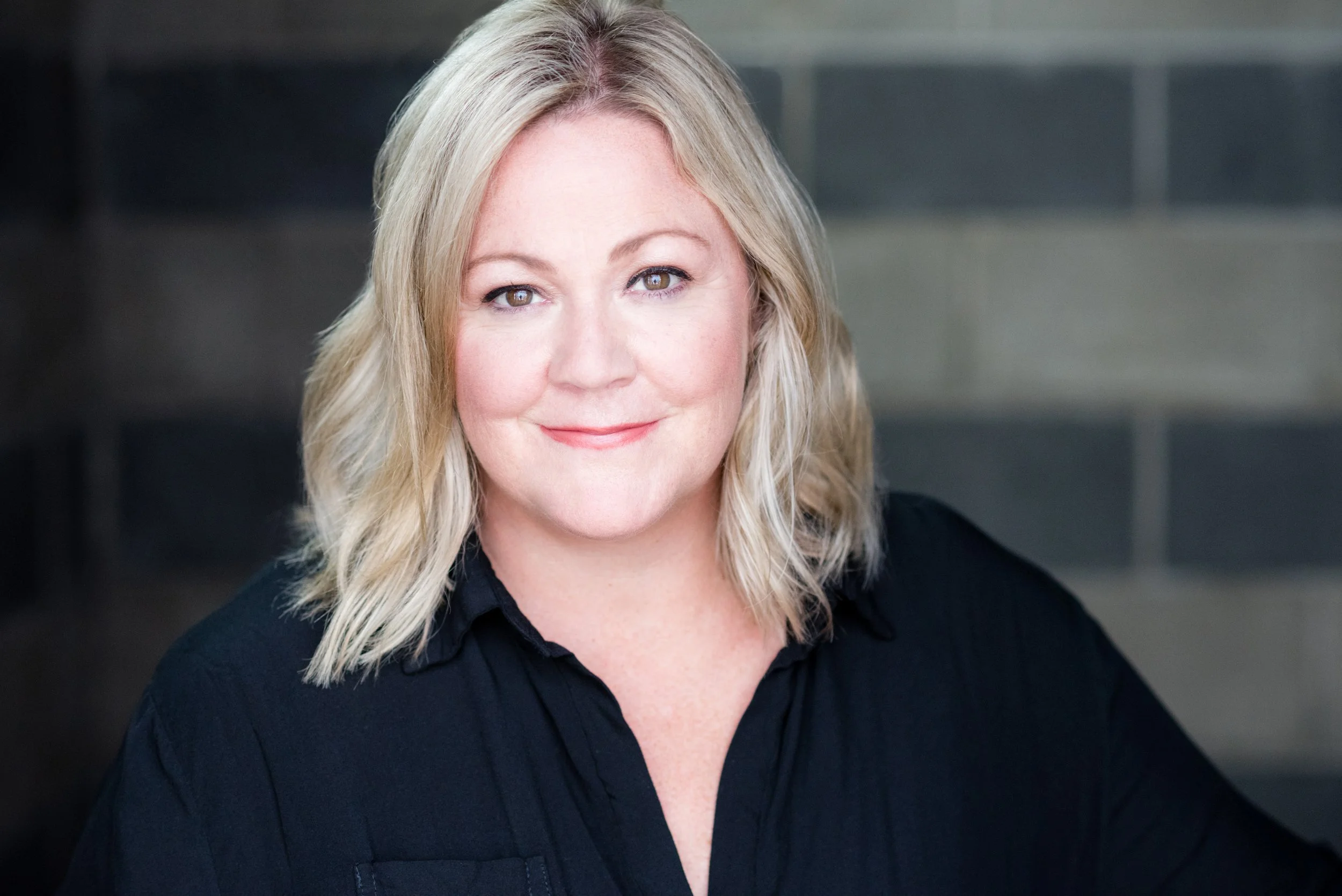 White woman with shoulder length blonde hair, wearing a black shirt.