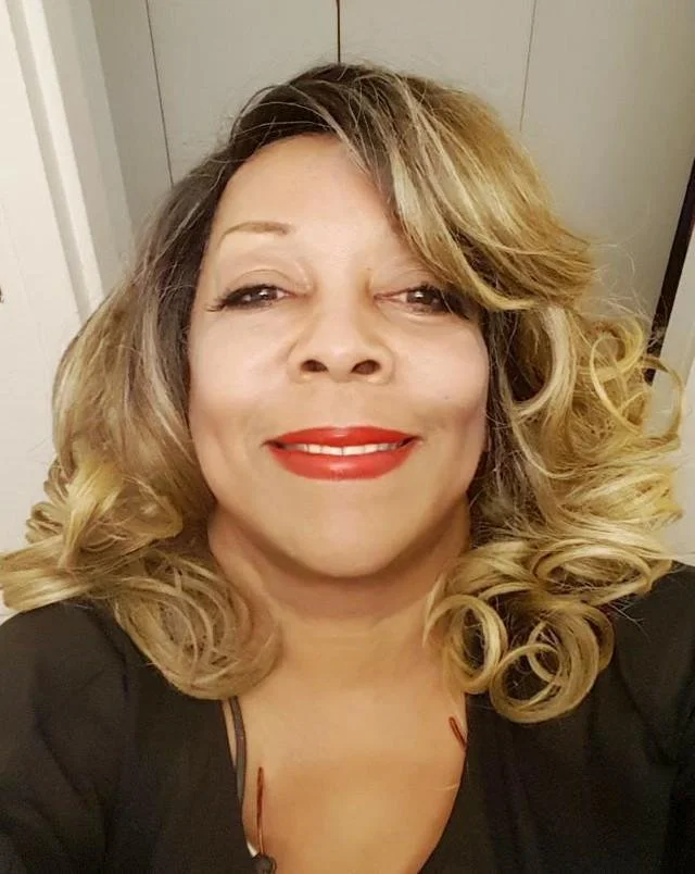 Black woman with blonde hair and red lips smiling to camera.