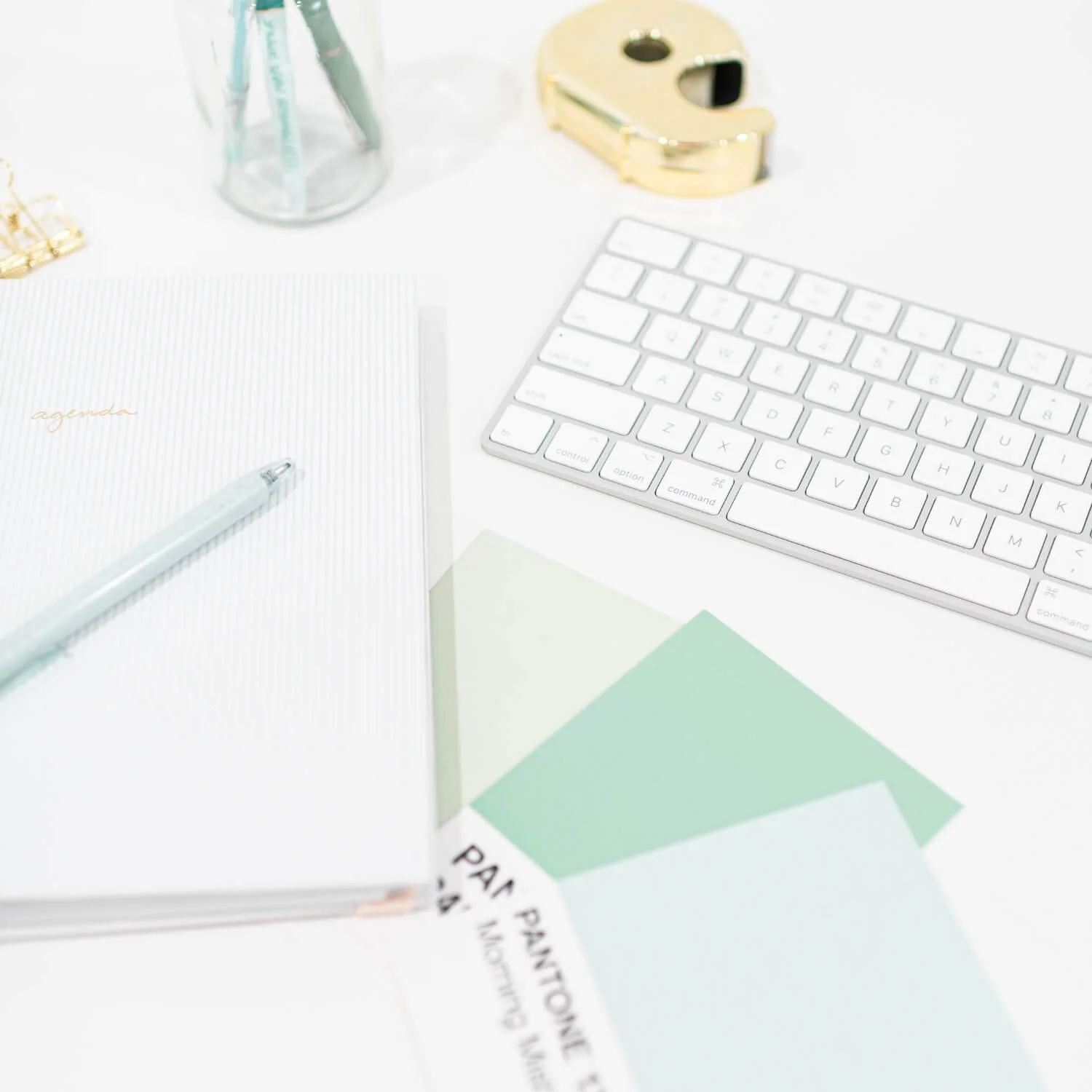A clean white desk setup with a keyboard, pastel notebook.jpg