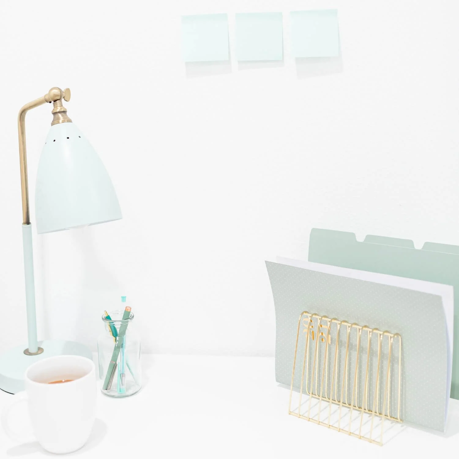 A tidy workspace featuring a mint desk lamp, cup of tea