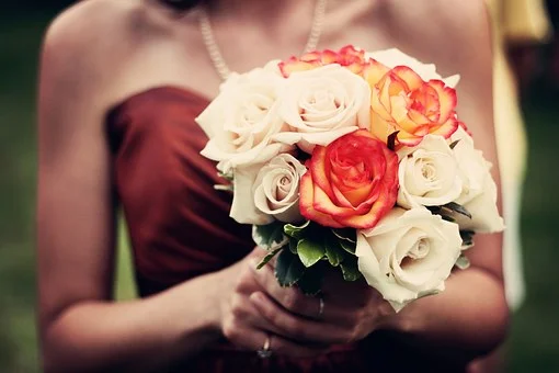 Person holding a bouquet of white, cream, and pink roses.