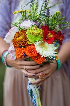 Person holding a colorful bouquet of flowers, including roses, carnations, and other blooms, with a neutral background.