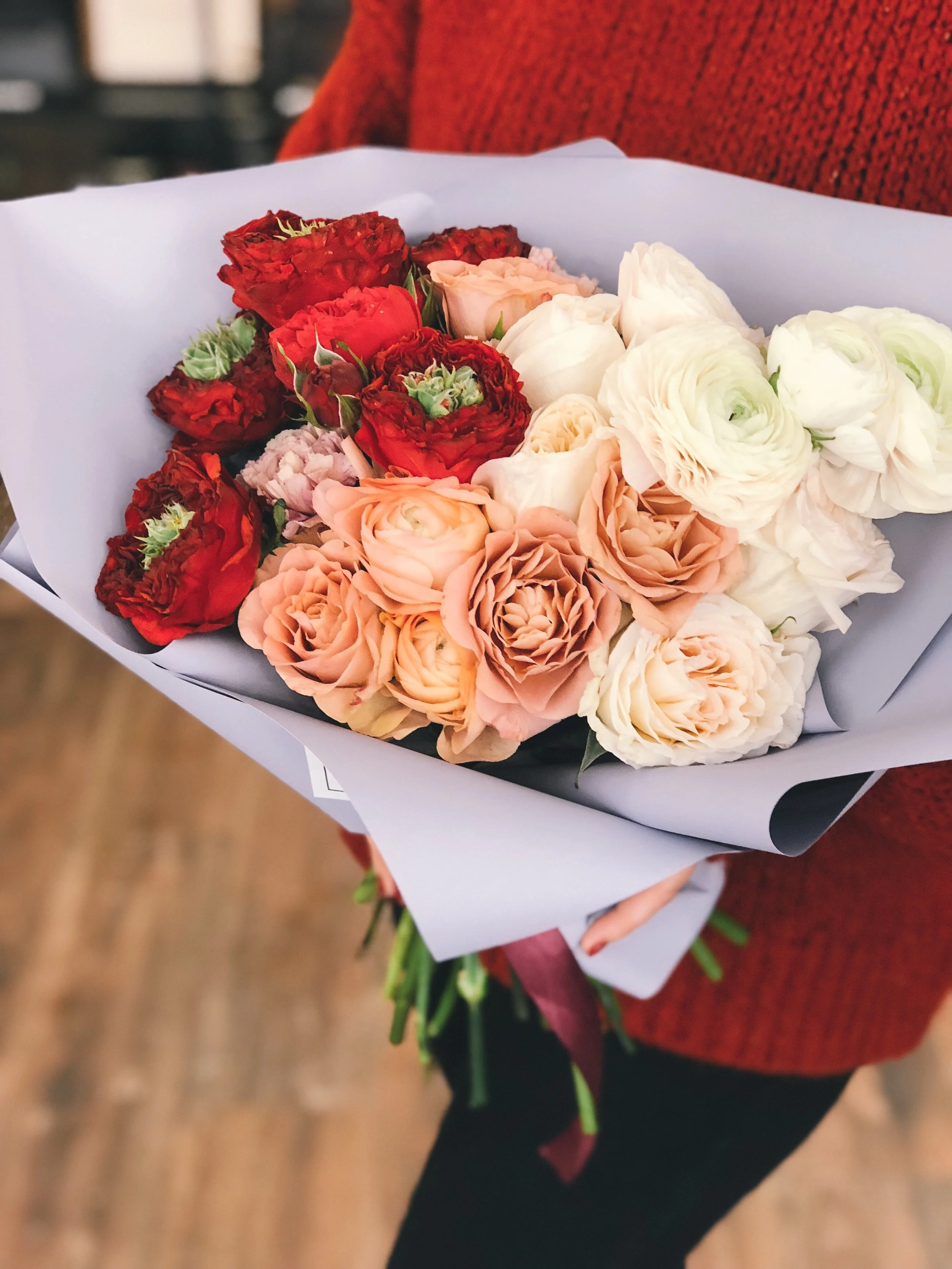 A bouquet of red, peach, white, and light pink flowers held by a person in a red sweater.