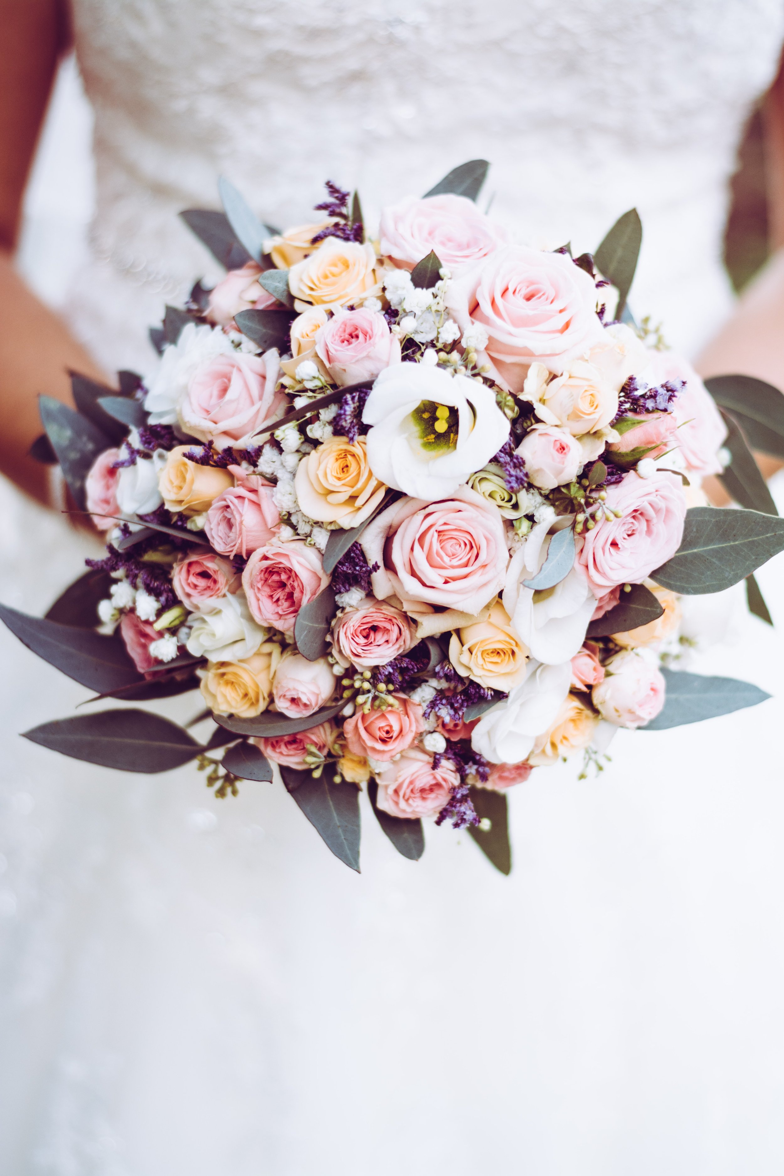 Bride holding a bouquet of pink, peach, white roses, calla lilies, and greenery.