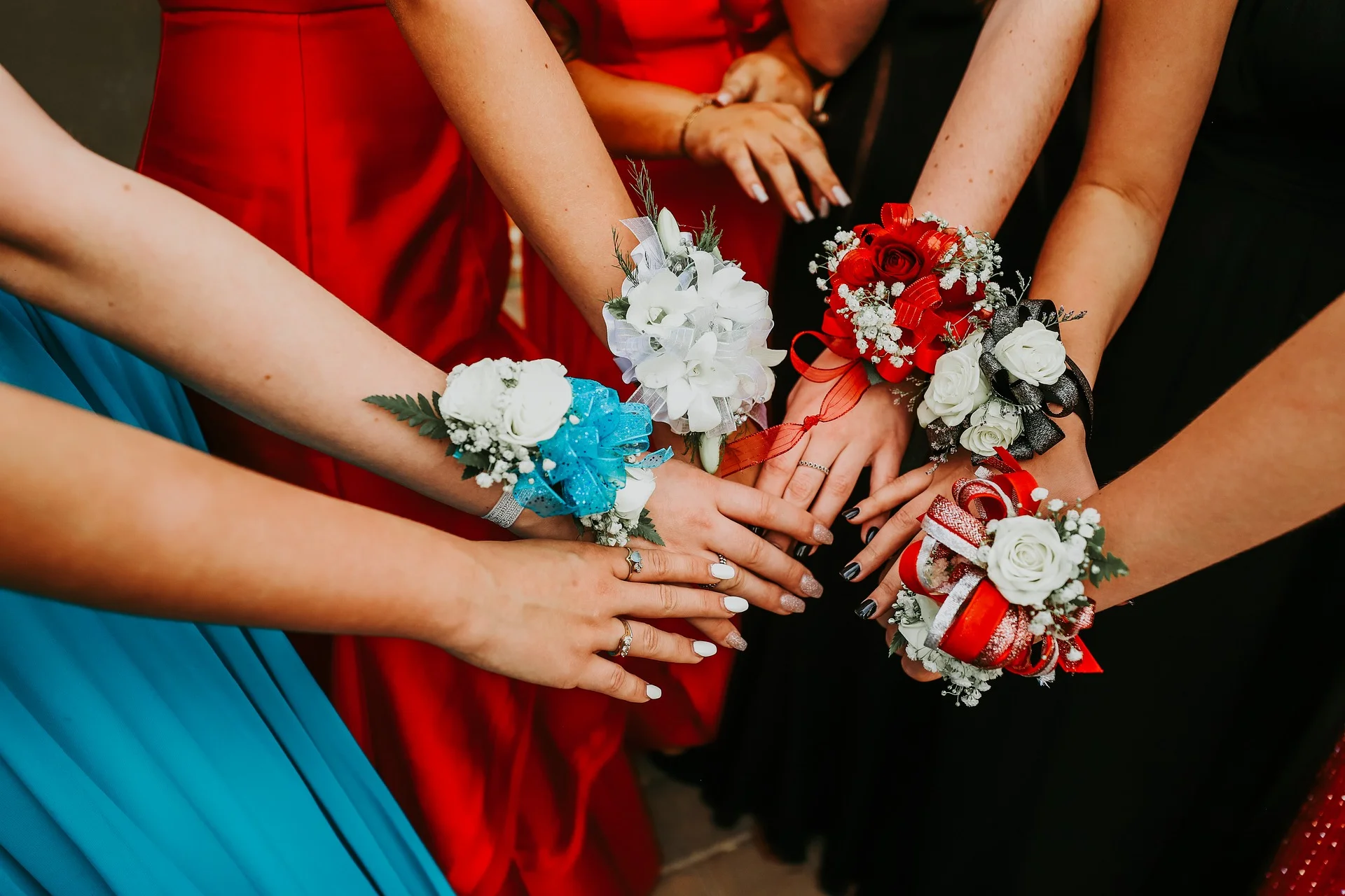 Group of women wearing colorful dresses with corsages on their wrists, placing their hands together in the center.
