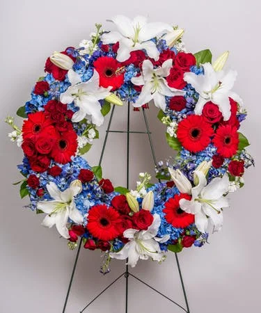 Red, white, and blue floral wreath with lilies, roses, and other flowers on a metal stand