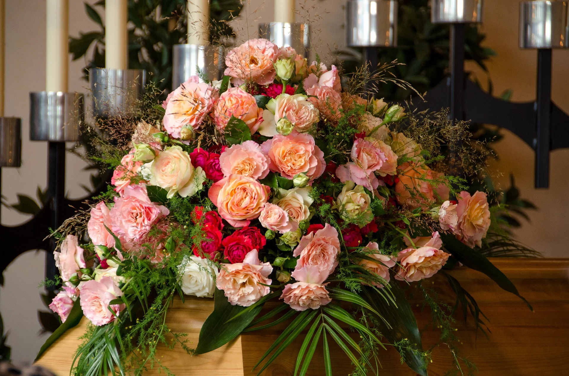 A large floral arrangement with pink, white, and red roses, including some peach-colored roses, set on a wooden surface with black candle holders in the background.