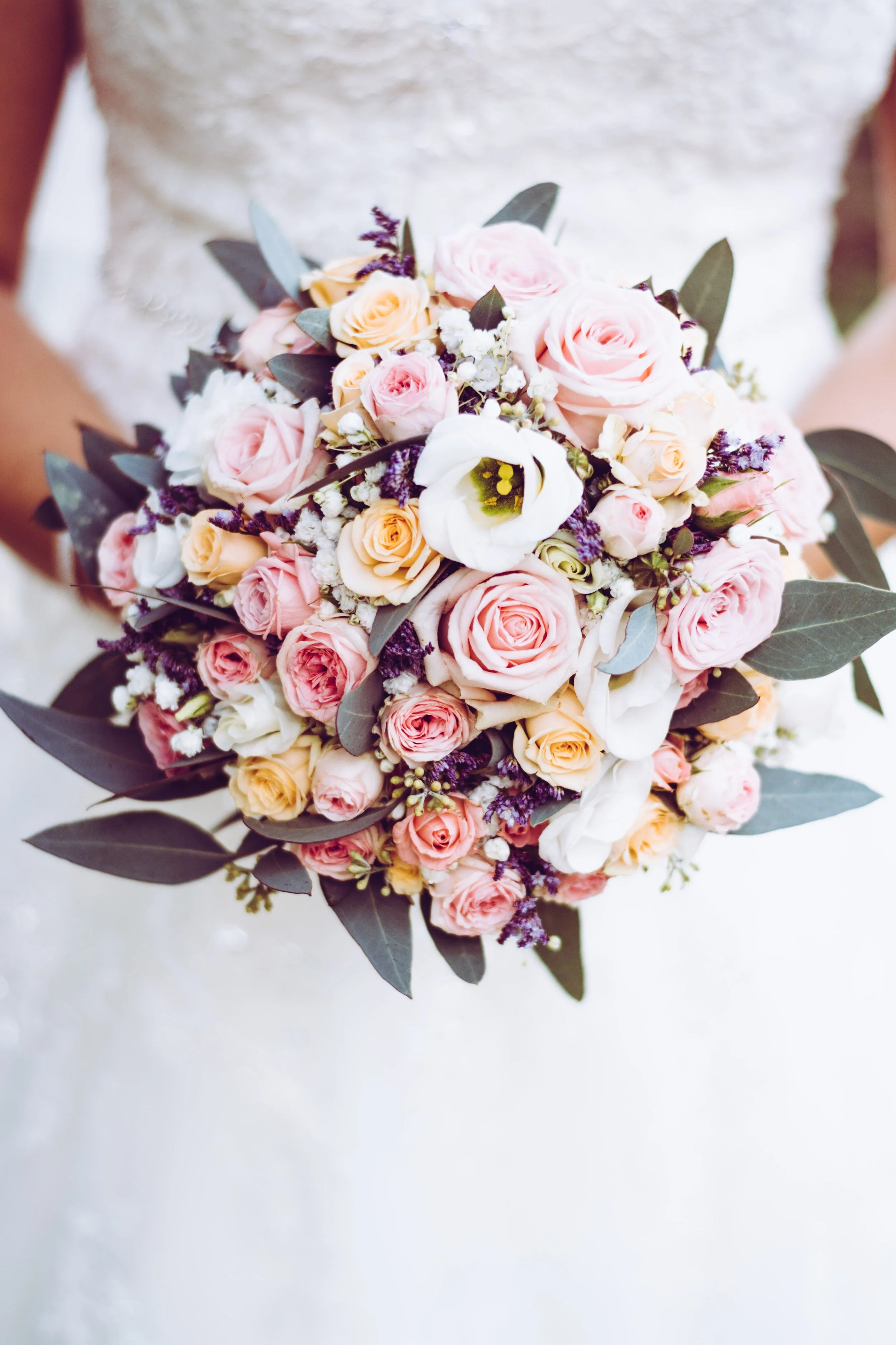 Bridal bouquet with pink, white, and peach roses, white calla lilies, and greenery.