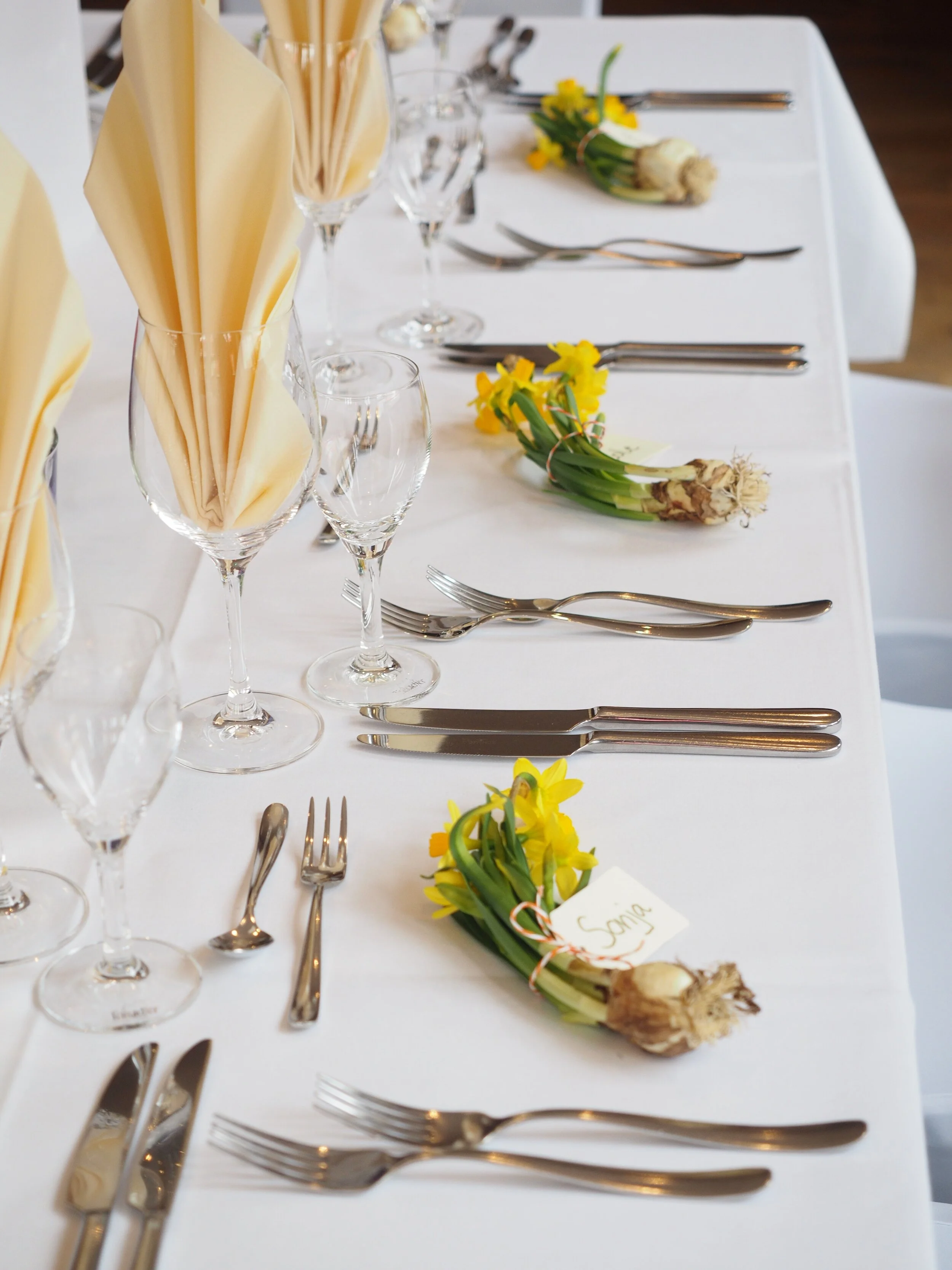 Formal dining table set with yellow flowers, napkins, and silverware.
