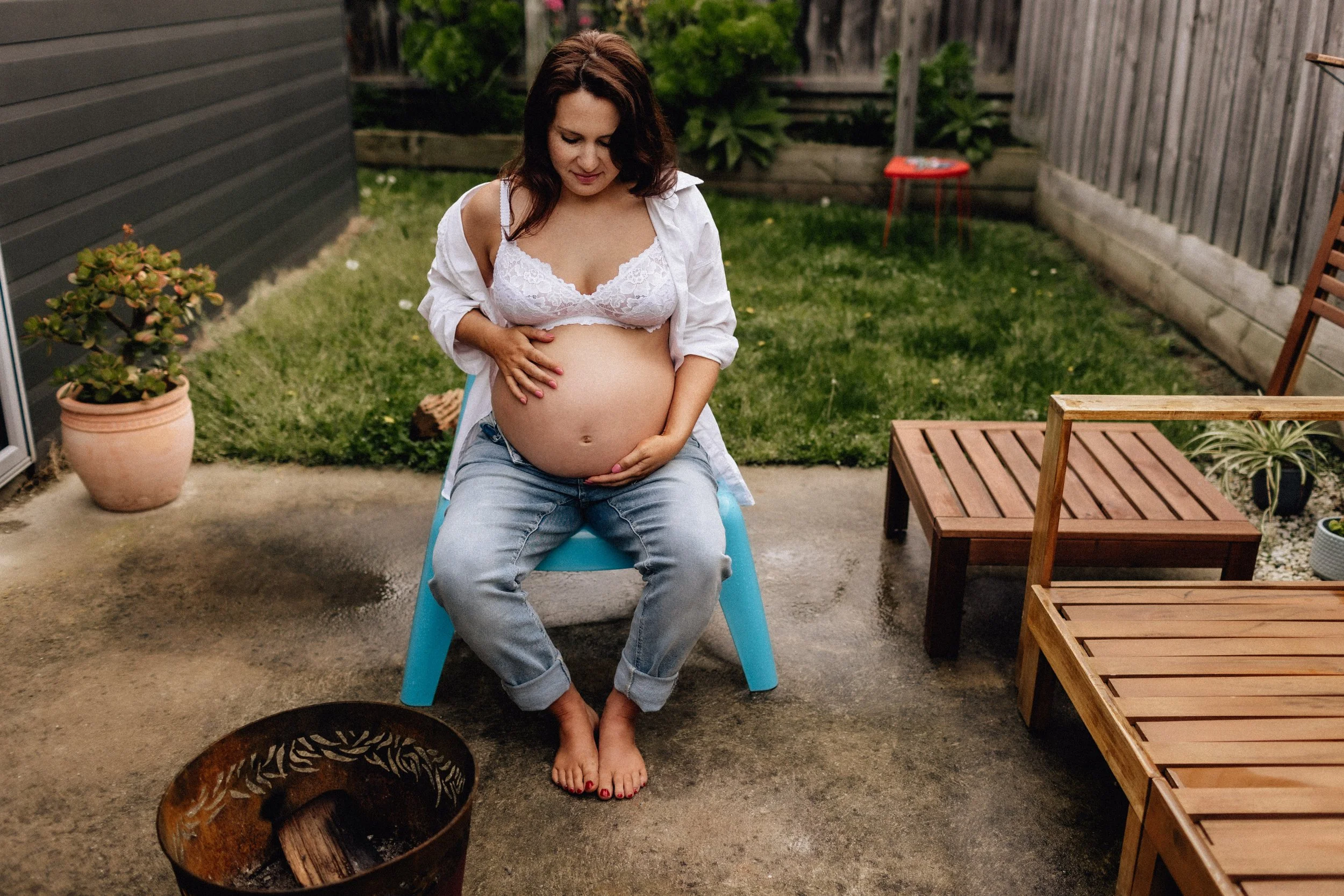 woman on blue deck chair in jeans and white shirt with pregnant tummy