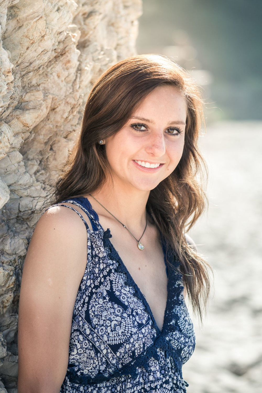Graduation portrait of a female student posing Against The seawall at Corona Del mar state beach