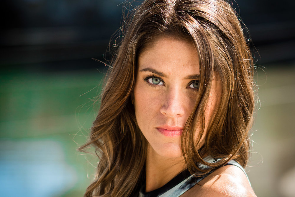 Headshot of personal trainer and OC booty camp founder nitro Nicki taken against a blue background at Balboa Harbor In Newport Beach