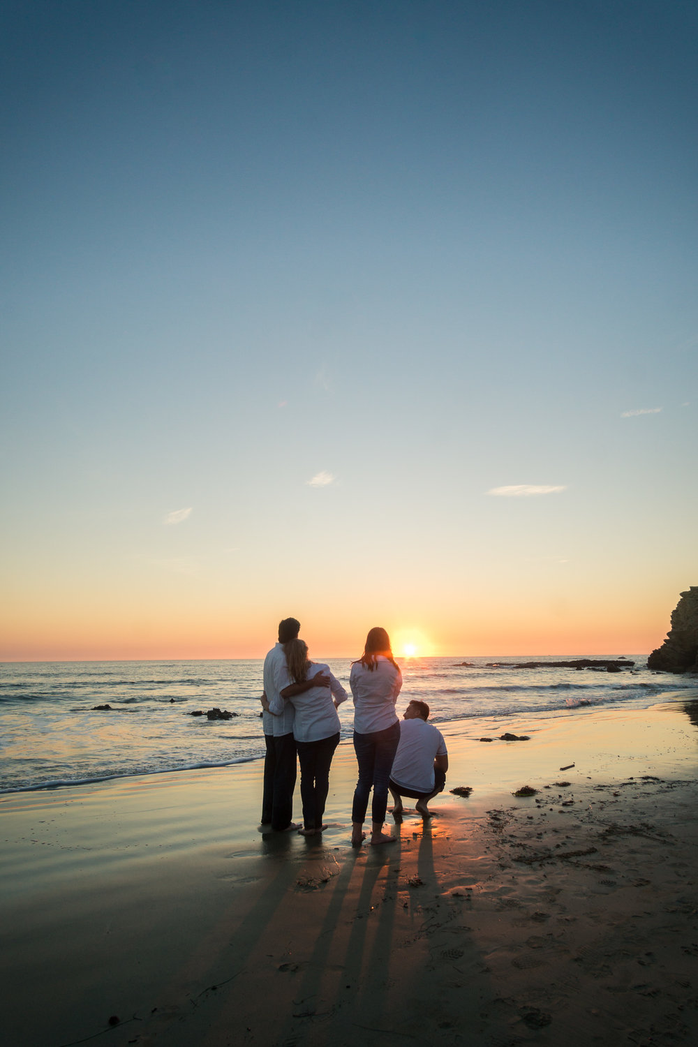 Family portraits of family walking on glassy seashore with blue sky and crescent moon while enjoying the sunset together during Golden hour at Crystal Cove State Beach in Newport