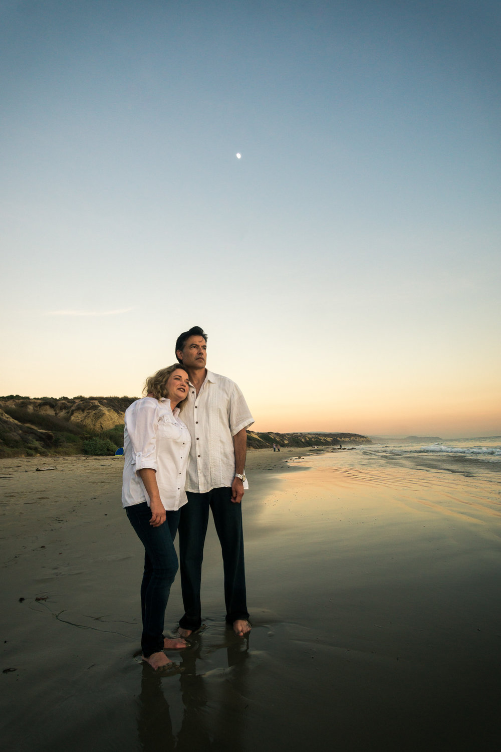 Family portraits of husband and wife with a  glassy seashore while enjoying the sunset together during Golden hour at Crystal Cove State Beach in Newport
