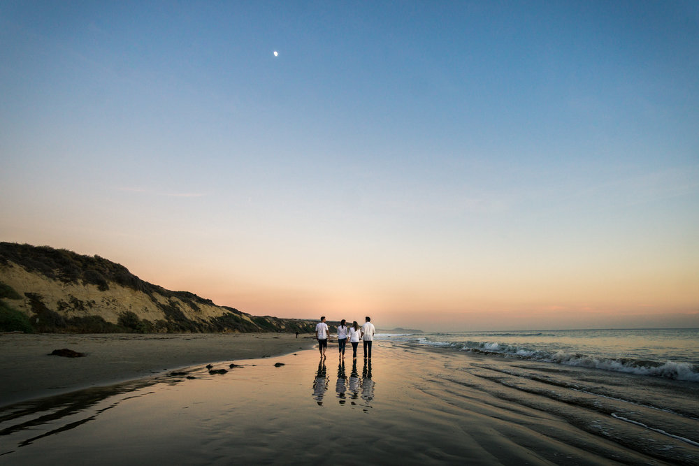 Family portraits of family walking on glassy seashore with blue sky and crescent moon while enjoying the sunset together during Golden hour at Crystal Cove State Beach in Newport