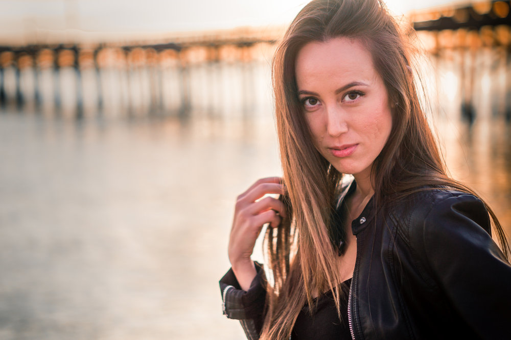 Natural light Fashion Portrait of female model wearing black leather jacket and blue jeans taken during Golden hour At Balboa Pier in Newport Beach