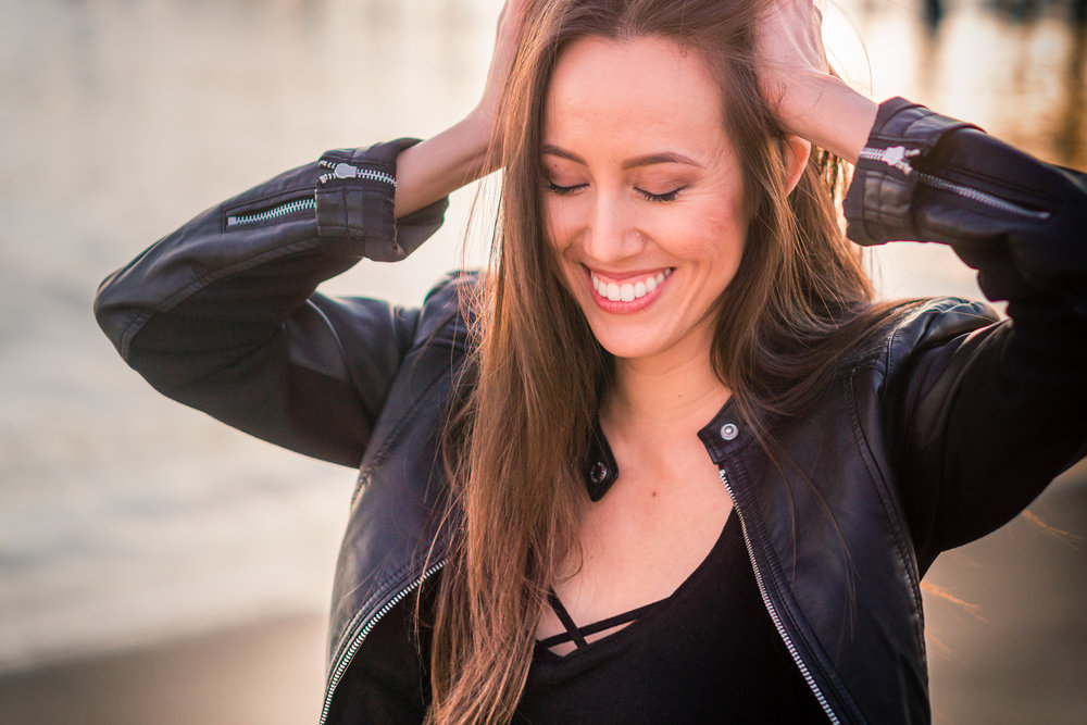 Natural light Fashion Portrait of smiling girl wearing black leather jacket and blue jeans taken during Golden hour At Balboa Pier in Orange County