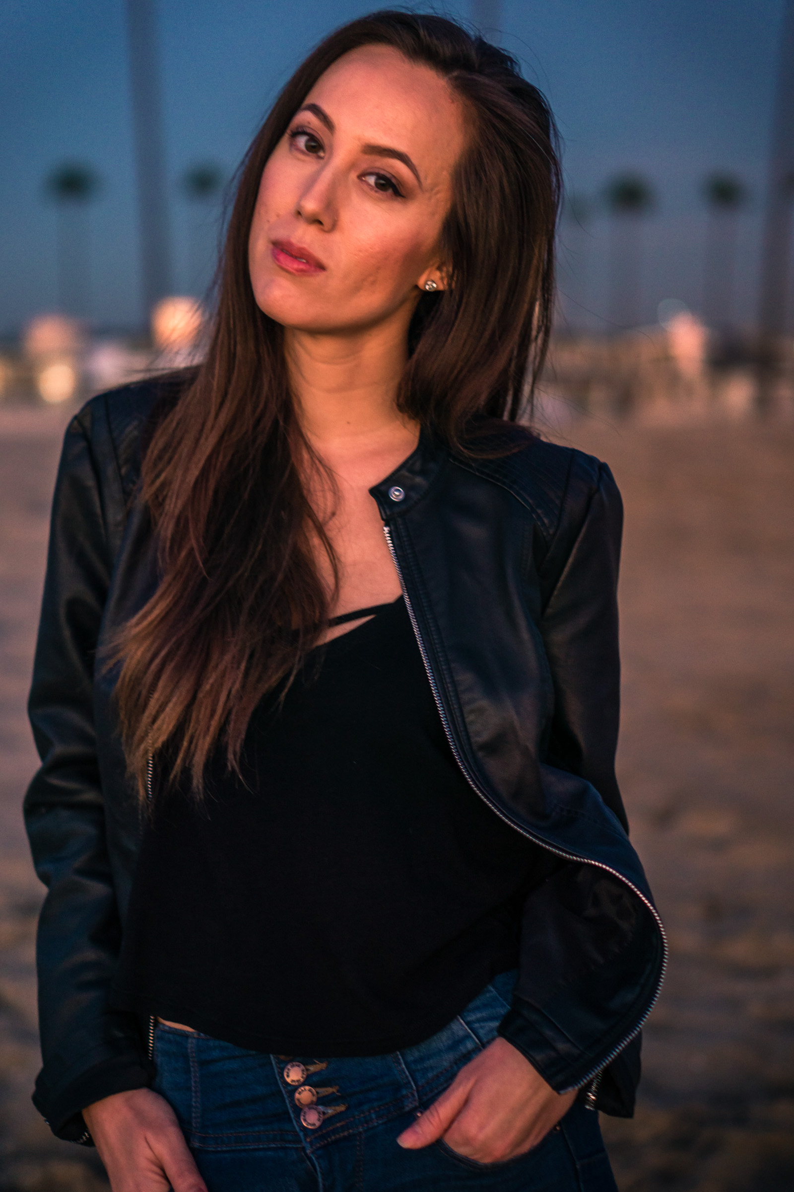 vibrant Natural light Fashion Portrait of woman posing in black leather jacket and blue jeans walking on beach during Golden hour At Balboa Pier in Newport Beach